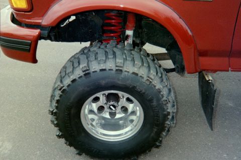 1995 Ford Bronco - Close-up of a red SUV's front wheel, showing a large off-road tire and suspension components.