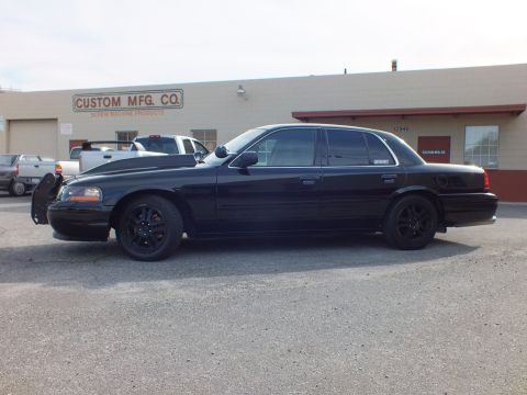 2003 Ford Crown Victoria - Driver-side profile of blacked-out Ford sedan with tinted windows and black five-spoke wheels.