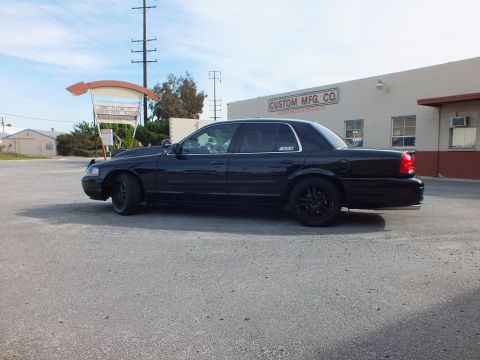 2003 Ford Crown Victoria - Profile of all-black full-size sedan, black wheels and dark tint, outside Custom Mfg Co.