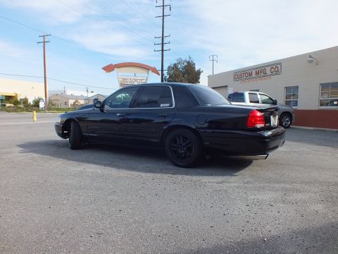 2003 Ford Crown Victoria - Blacked-out Ford sedan rear quarter view with red taillights, parked at Custom Mfg Co.
