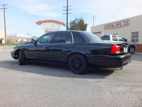 2003 Ford Crown Victoria - Murdered-out full-size sedan rear quarter, dual exhaust and tinted glass, in a paved lot.