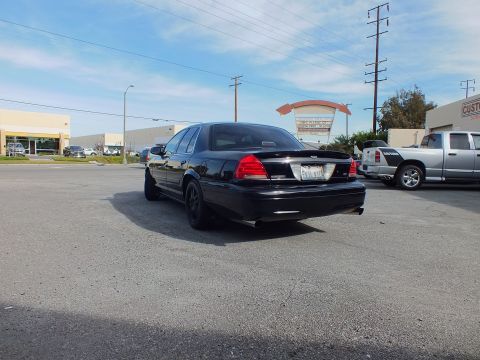 2003 Ford Crown Victoria - Murdered-out full-size sedan from behind with red taillights and lip spoiler under blue sky.