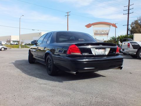2003 Ford Crown Victoria - Blacked-out Ford sedan rear quarter, dual exhaust and EVIL VIC plate, in a paved lot.