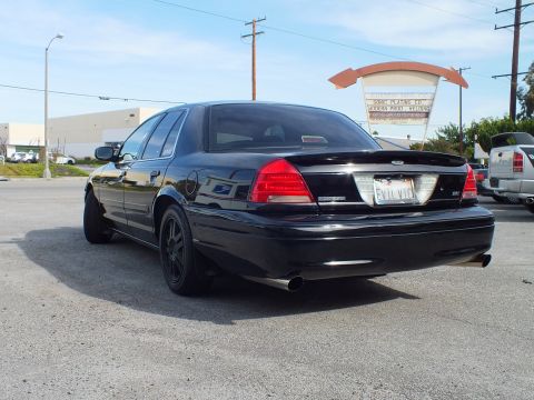 2003 Ford Crown Victoria - Murdered-out sedan from behind showing INTERCEPTOR trunk script and dual exhaust tips.