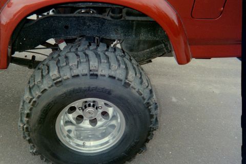 1995 Ford Bronco - A red SUV is shown from the side, focusing on its large off-road tire and fender.