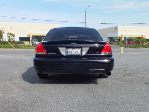 2003 Ford Crown Victoria - Blacked-out full-size sedan rear, Ford oval, dual exhaust and red taillights, paved lot.