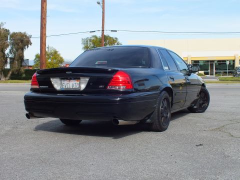 2003 Ford Crown Victoria - Blacked-out full-size sedan rear quarter, dual exhaust and lip spoiler, on sunny pavement.