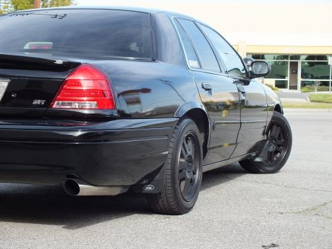 2003 Ford Crown Victoria - Rear three-quarter close-up of a blacked-out sedan showing SVT trunk badge, chrome dual tips and black wheels