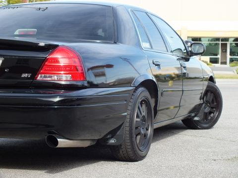 2003 Ford Crown Victoria - Tight rear quarter view of a blacked-out sedan, SVT badge and chrome exhaust tip visible against gloss black body