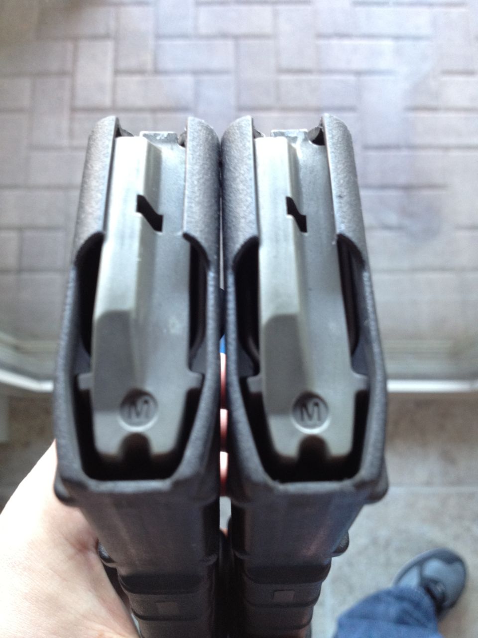 Two black gun magazines held in hand, showing the top feed mechanism