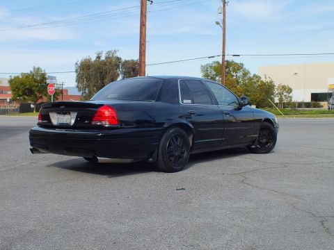 2003 Ford Crown Victoria - Blacked-out sedan photographed from rear quarter, SVT badge and black aftermarket wheels in view