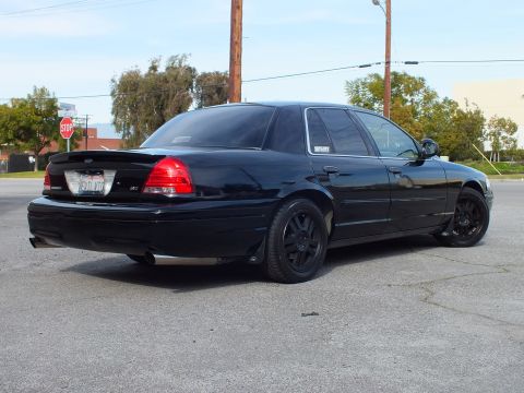 2003 Ford Crown Victoria - Rear three-quarter of a gloss black sedan on cracked pavement, California plate and dark wheels shown