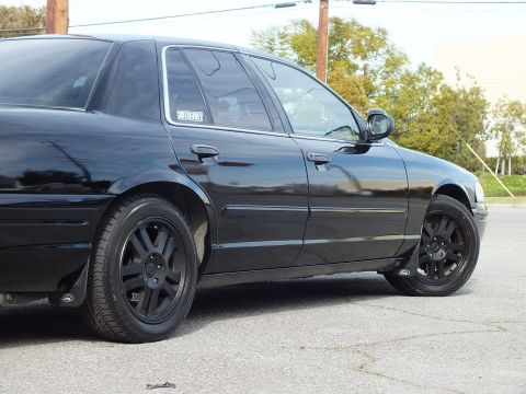 2003 Ford Crown Victoria - Close side-rear view of a blacked-out sedan, chrome rocker trim and black wheels against the bodywork