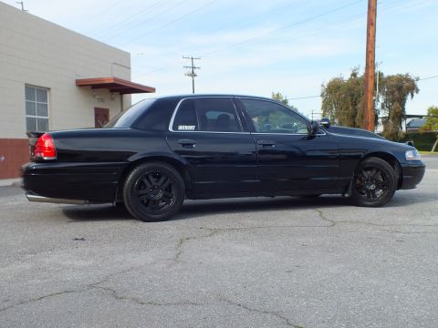 2003 Ford Crown Victoria - Side profile of a lowered blacked-out sedan on black wheels, parked along a building wall