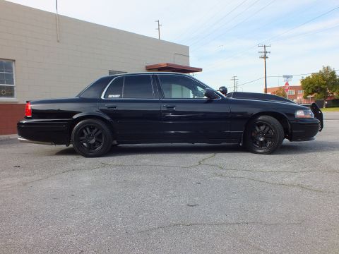 2003 Ford Crown Victoria - Side view of a gloss black lowered sedan parked on cracked pavement near a building