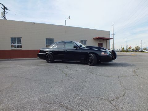 2003 Ford Crown Victoria - Front three-quarter view of a blacked-out sedan sitting low on a wide empty parking lot