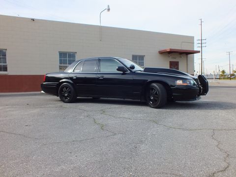2003 Ford Crown Victoria - Blacked-out sedan from front quarter showing a chrome push bar and bright projector headlights