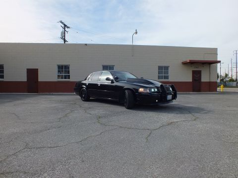 2003 Ford Crown Victoria - Blacked-out sedan parked at an angle, push bar and illuminated headlights facing camera
