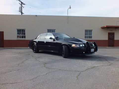 2003 Ford Crown Victoria - Front quarter of a lowered blacked-out sedan with push bar and glowing projector headlights