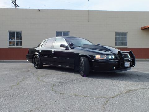 2003 Ford Crown Victoria - Blacked-out sedan from the front quarter, chrome push bar and California plate visible