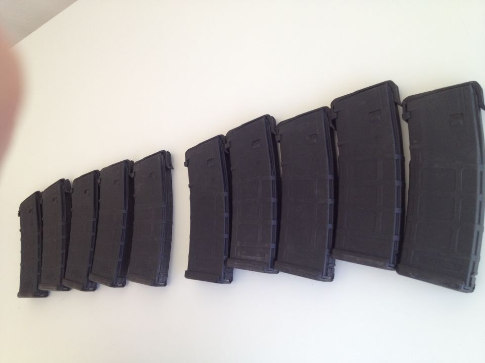 Several black gun magazines lined up on a white wall