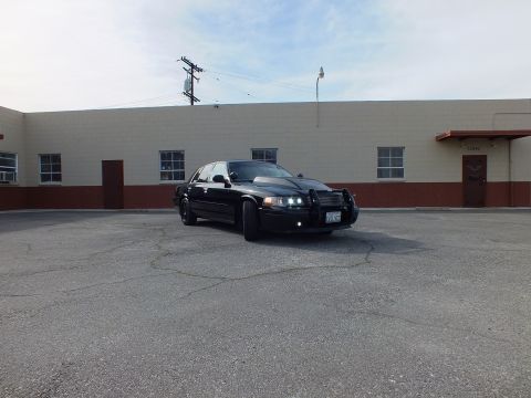 2003 Ford Crown Victoria - Distant front-quarter view of a blacked-out sedan with push bar in a large empty lot