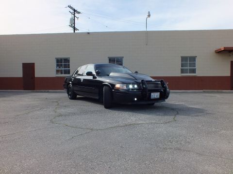 2003 Ford Crown Victoria - Front quarter of a blacked-out sedan with push bar, California plate and lit headlights