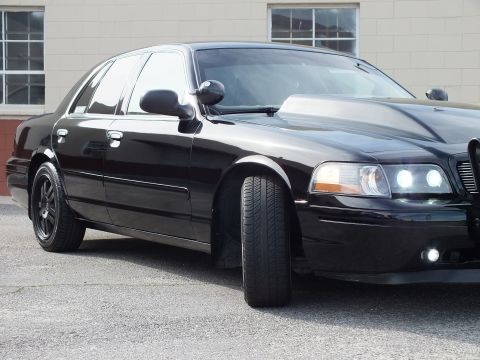 2003 Ford Crown Victoria - Close front-side view of a blacked-out sedan, chrome grille and bright projector headlight visible