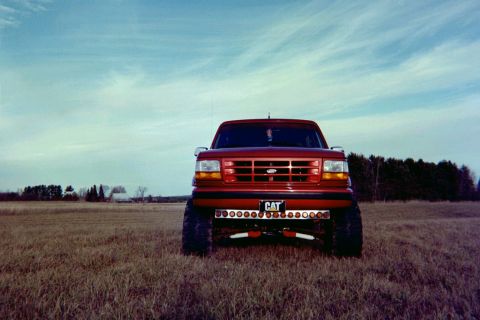 1995 Ford Bronco - A red Ford F-Series truck is parked in a field under a cloudy sky.