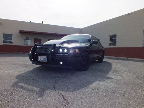 2003 Ford Crown Victoria - Front-quarter of the black Crown Vic, billet grille and grille guard, HIDs glowing in afternoon light.