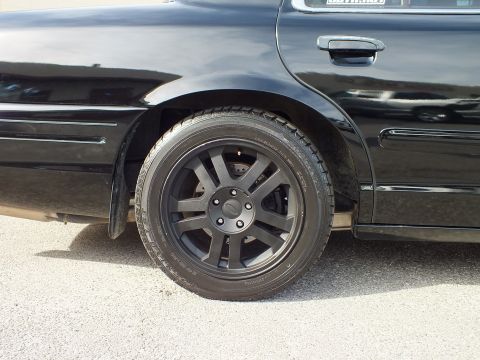 2003 Ford Crown Victoria - Side detail of the rear matte-black wheel and low-profile tire on the black Crown Victoria.