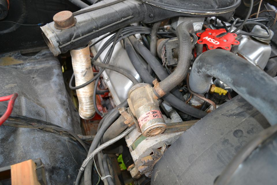 Engine bay with radiator hose, distributor cap, and fuel filter visible. Some text on the fuel filter is readable