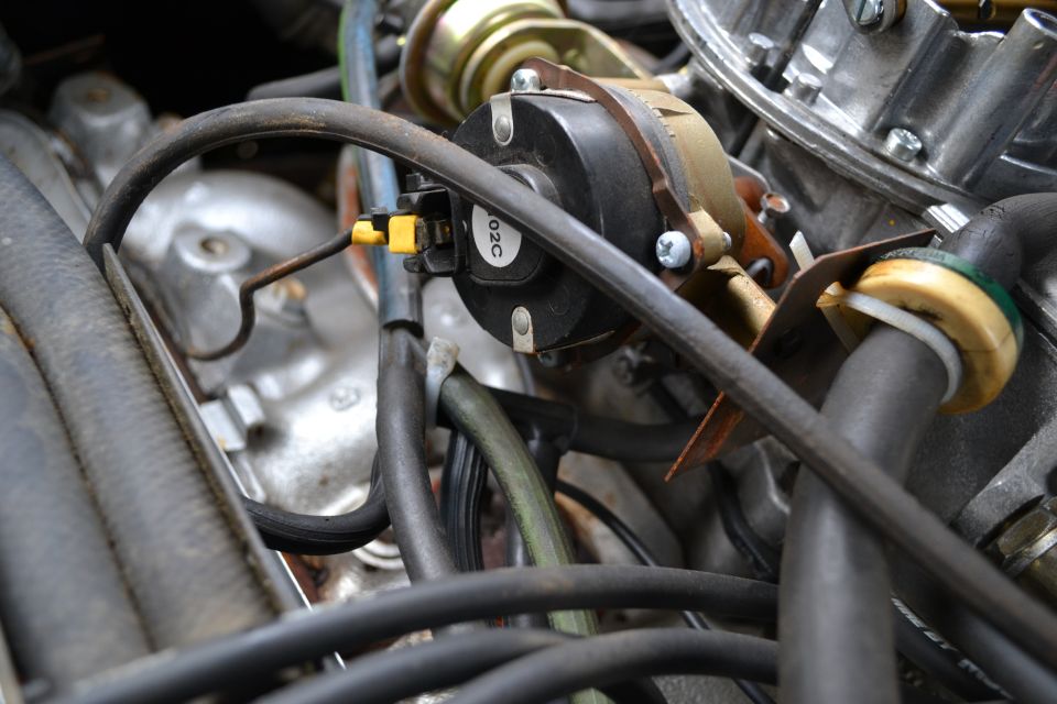 Close-up of engine carburetor with hoses and a black component labeled 02C