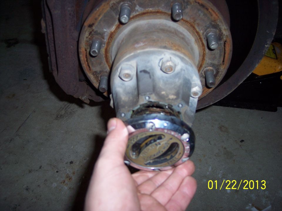 hand holding a chrome locking hub near a rusty wheel hub assembly