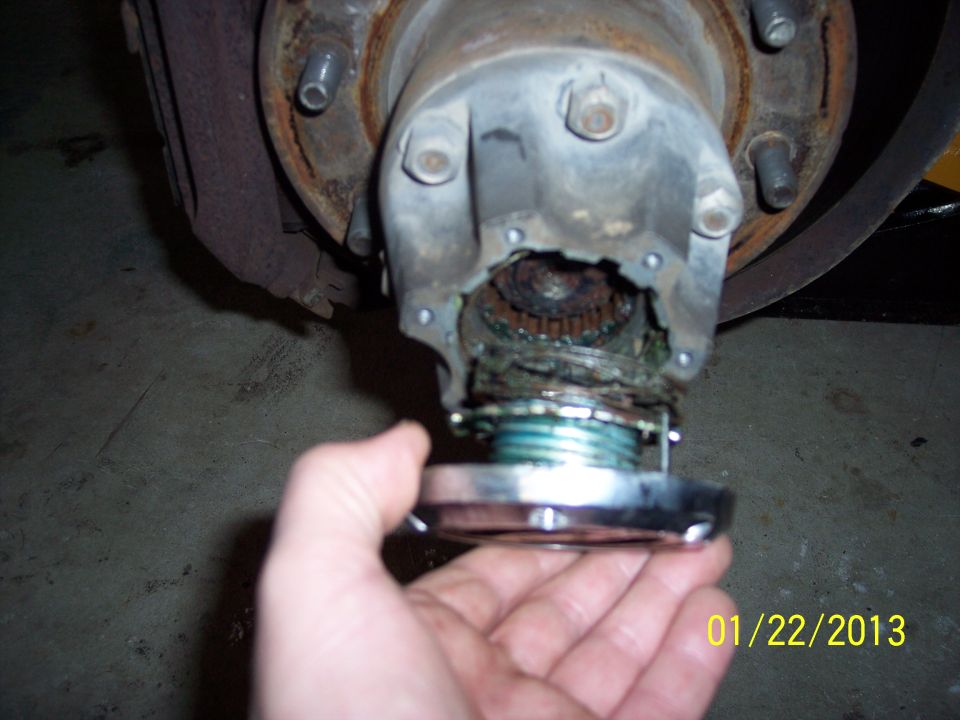 Hand holding chrome locking hub over damaged front wheel hub assembly with exposed gears and grease
