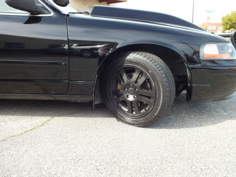 2003 Ford Crown Victoria - Front wheel and fender detail of the black Crown Victoria with matte multi-spoke rim and low-profile tire.