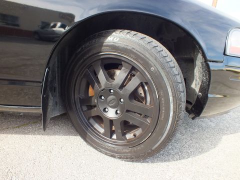 2003 Ford Crown Victoria - Rear wheel close-up of the black Crown Vic, Ford-capped matte rim wrapped in a Toyo tire.