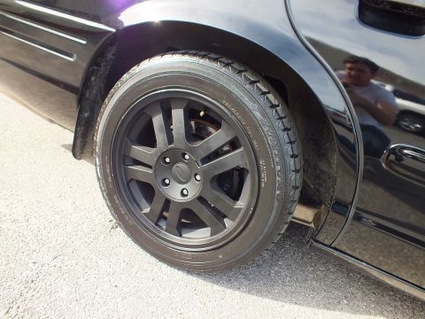 2003 Ford Crown Victoria - Rear wheel detail of the dark Crown Vic, a person reflected in the glossy fender behind the tire.