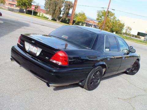 2003 Ford Crown Victoria - Rear three-quarter of the blacked-out Crown Vic showing the trunk badge, black wheels and dual exhaust tips.