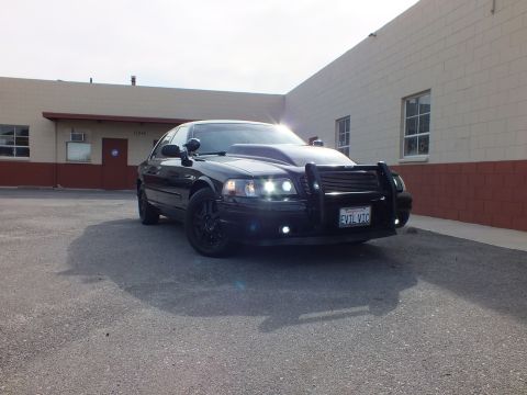 2003 Ford Crown Victoria - Front-corner shot of the black Interceptor, grille guard and HIDs lit, EVIL VIC California plate showing.