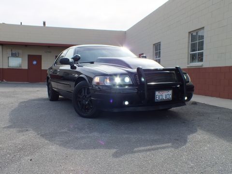 2003 Ford Crown Victoria - Front-quarter of the blacked-out Crown Vic, push bar and grille, projector HIDs glowing in the sun.
