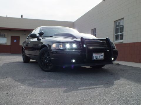 2003 Ford Crown Victoria - Front-corner view of the dark Interceptor with grille guard, HIDs and the EVIL VIC plate centered.