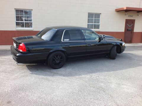 2003 Ford Crown Victoria - Rear three-quarter view of a blacked-out Crown Victoria parked near a red metal door marked 12942.