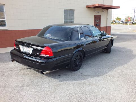 2003 Ford Crown Victoria - Tail end of a black Crown Victoria with Ford oval, dual exhaust and dark tint on a sunny lot.