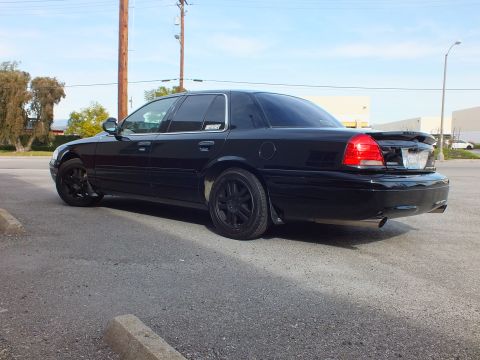 2003 Ford Crown Victoria - Lowered black Crown Victoria from the rear left under power lines and clear sky.