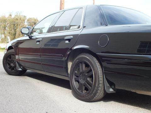 2003 Ford Crown Victoria - Close passenger-side detail of a black Crown Victoria showing fuel door and Ford mud flaps.