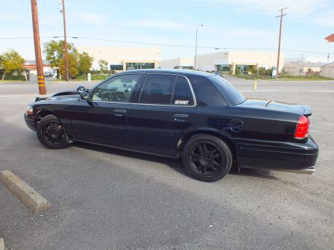 2003 Ford Crown Victoria - Black Crown Victoria parked rear-on in a lot with a glass-front commercial building behind.
