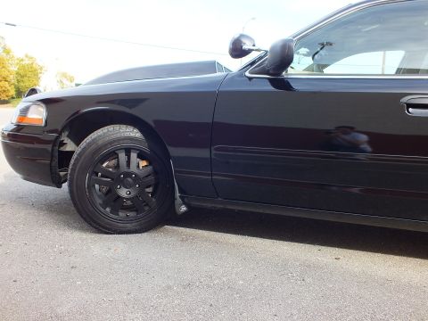 2003 Ford Crown Victoria - Tight front fender and wheel detail of a dark Crown Victoria with side mirror in frame.