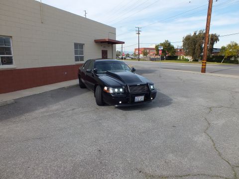 2003 Ford Crown Victoria - Distant front three-quarter of a black Crown Victoria with brush guard near a building.