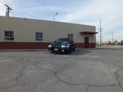 2003 Ford Crown Victoria - Black Crown Victoria with headlights on photographed across a large cracked parking lot.
